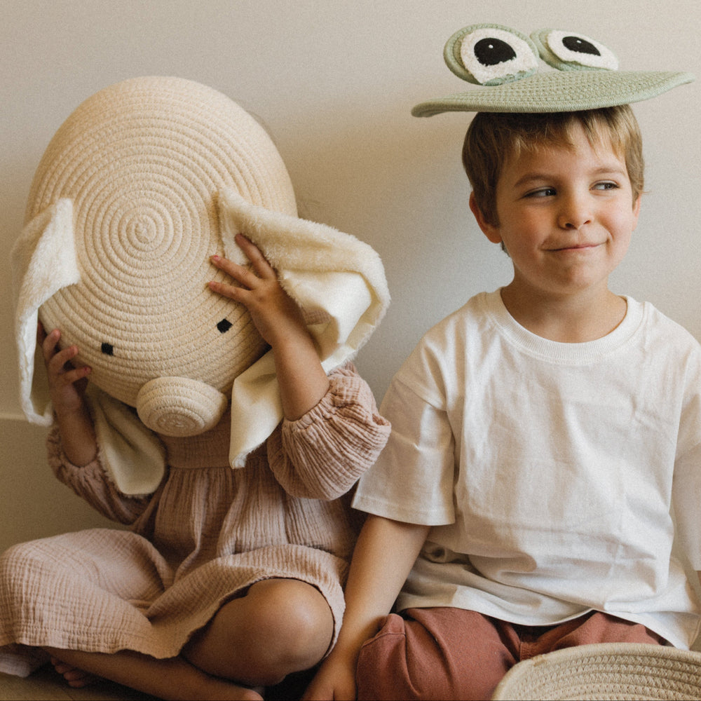 Two children playing with a large stuffed animal and a hat shaped like a frog.